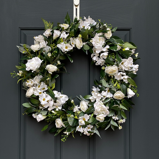 Handcrafted by Darling Grape / Emily Allen. This high-end, artificial spring front door wreath has been handcrafted on a grapevine base and is filled with dogwood blossoms, ranunculus, and lisianthus and accented with mini floral sprays and green berries. Florals are nestled in various greenery, including osmanthus, pittosporum, and eucalyptus.