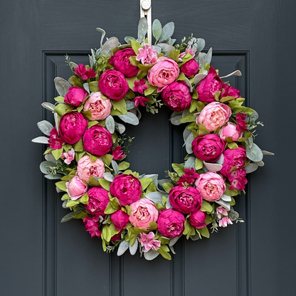 A pink peony and lambs ear wreath handcrafted on a grapevine base, displayed on a dark door.