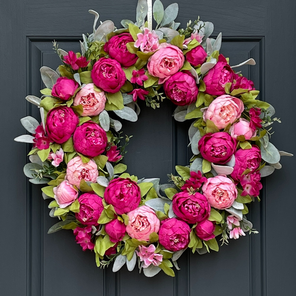 A pink peony and lambs ear wreath handcrafted on a grapevine base, displayed on a dark door.