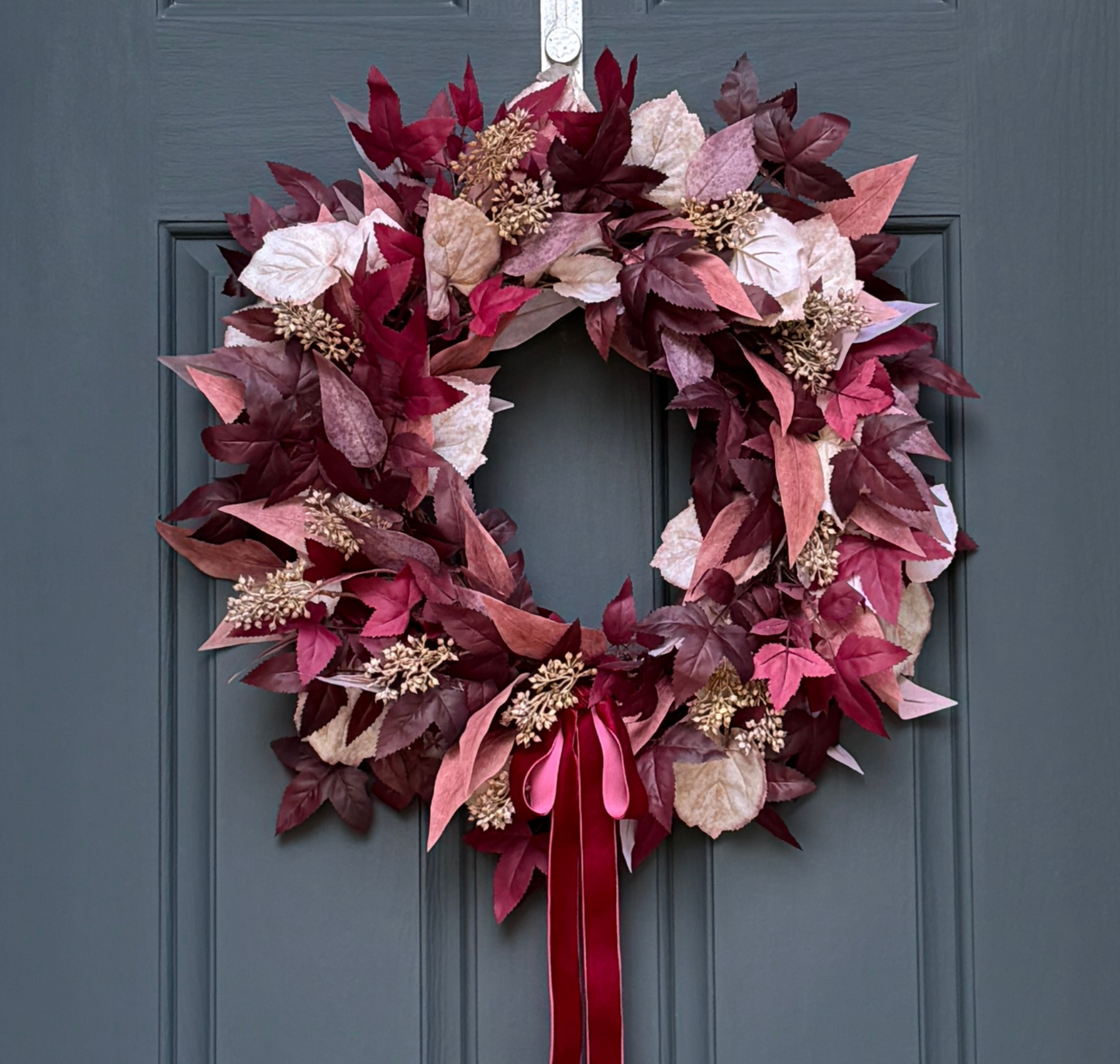 Burgundy and cream fall wreath with plum leaves, berries, and a dark red velvet bow on a grapevine base for autumn front door décor.