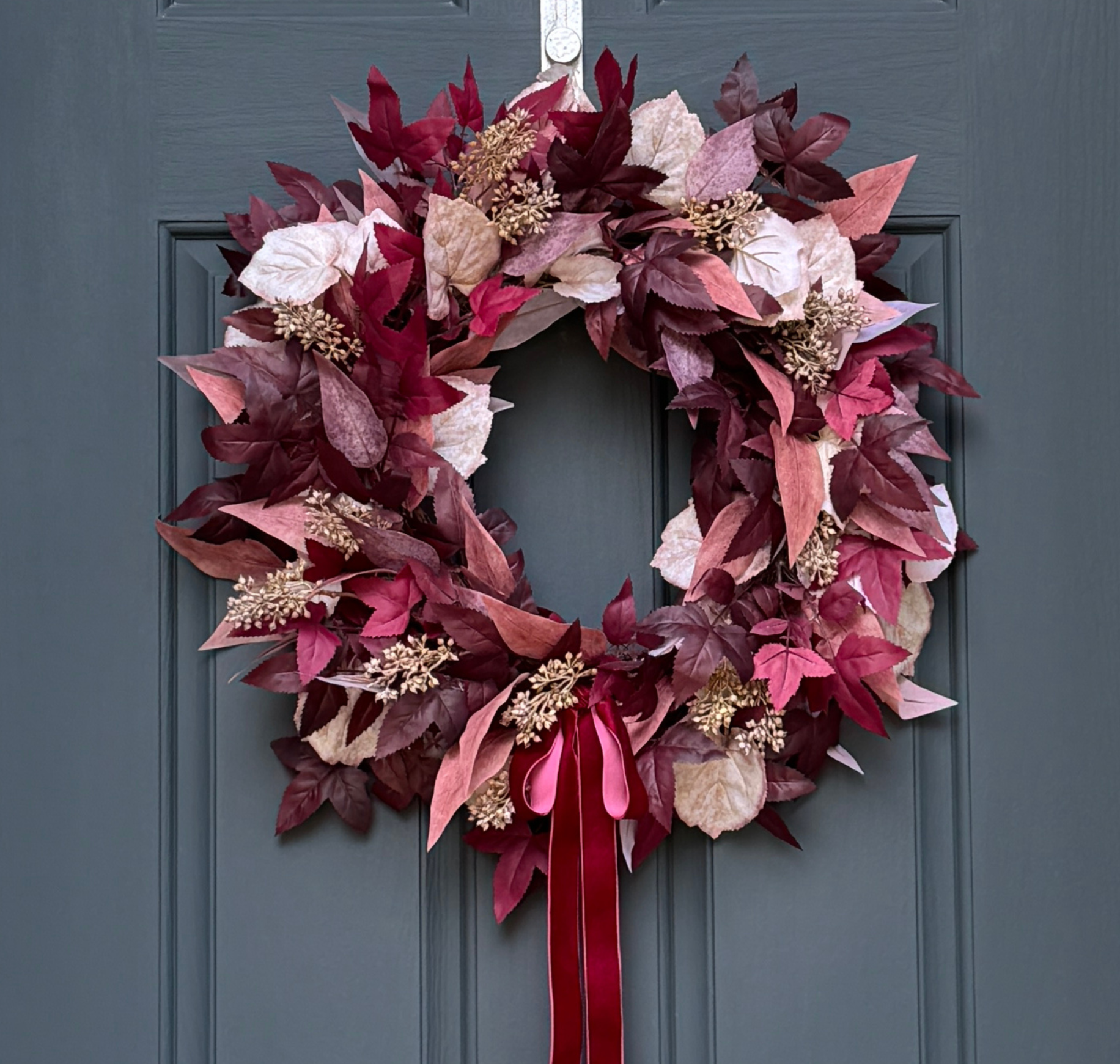 Burgundy and cream fall wreath with plum leaves, berries, and a dark red velvet bow on a grapevine base for autumn front door décor.