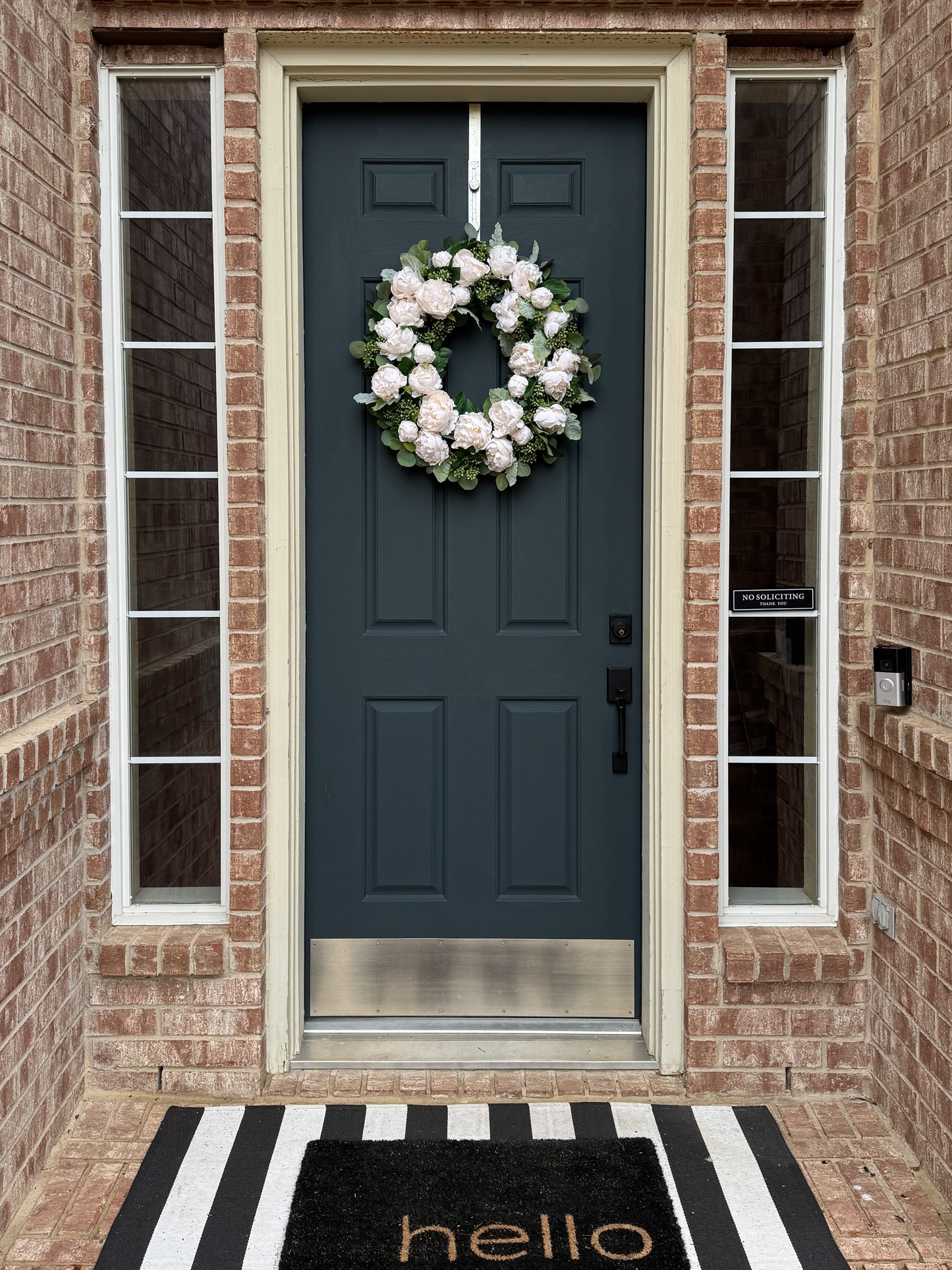 Blue front door with a white wreath, black and white striped rug, and 'hello' mat.