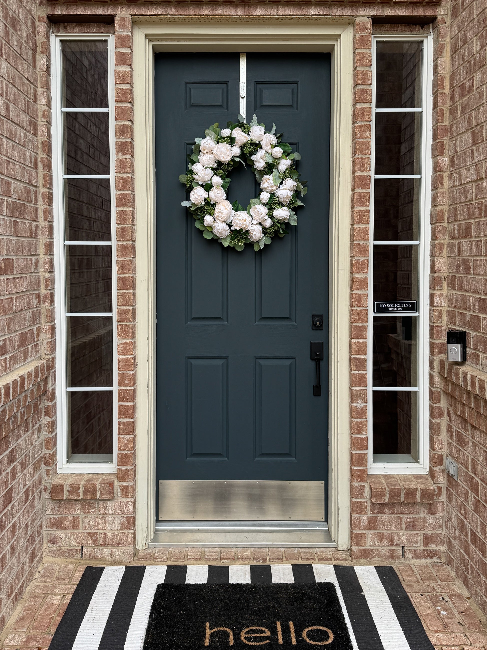 Blue front door with a white wreath, black and white striped rug, and 'hello' mat.