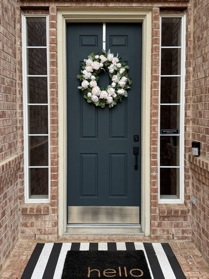 Blue front door with a white wreath, black and white striped rug, and 'hello' mat.