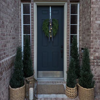 Front door of a house with a wreath, flanked by potted plants and lanterns.