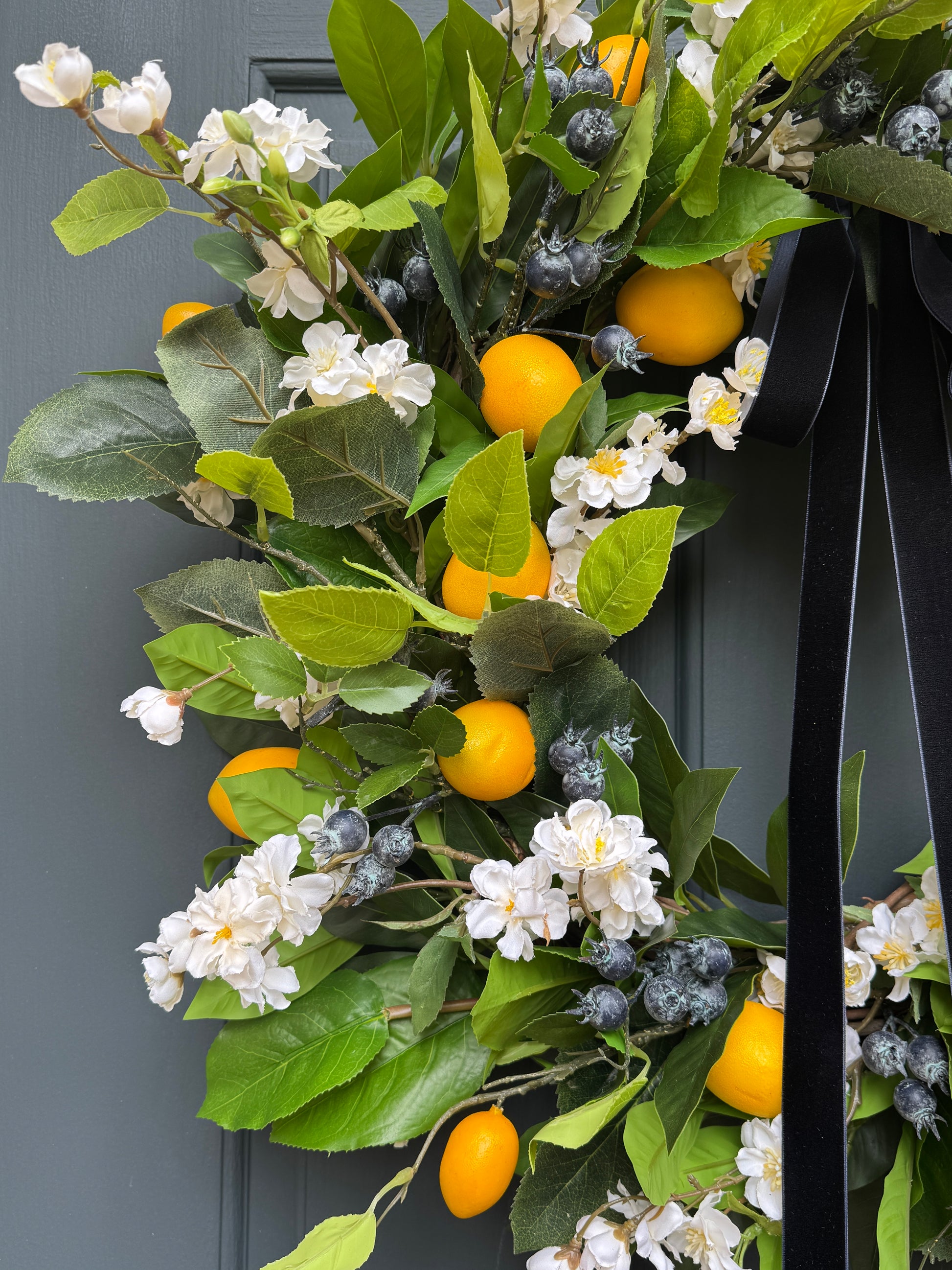 Decorative wreath with green leaves, white flowers, and yellow fruits on a dark background