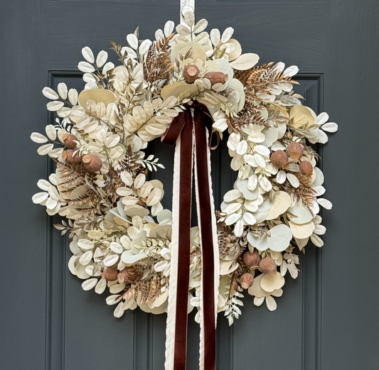 Neutral fall eucalyptus wreath with beige leaves, brown poppy pods, ferns, brushed gold accents, and brown velvet ribbon for front door décor.