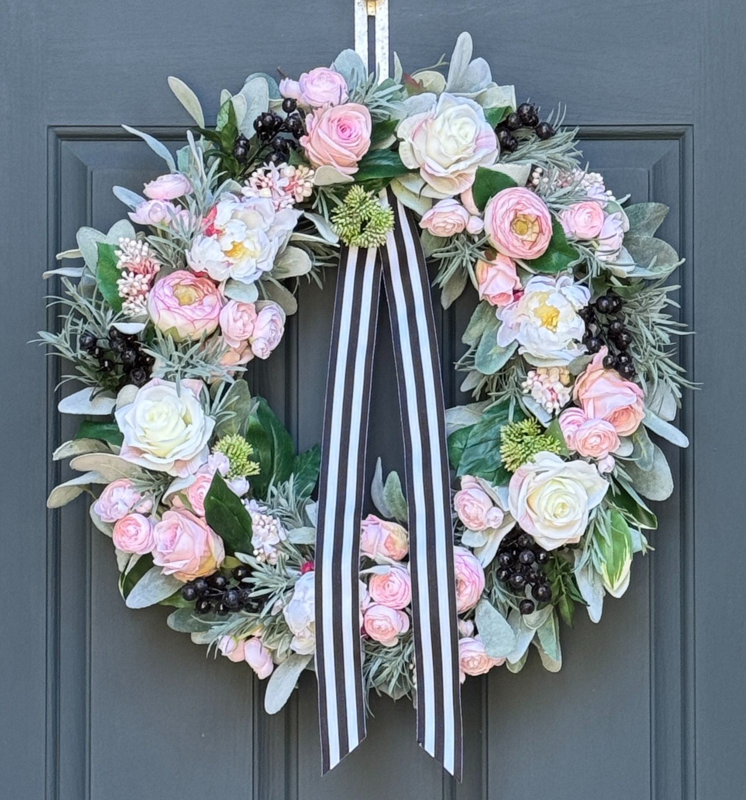 Peony, rose, and ranunculus wreath with pink and cream flowers, greenery, navy berries, and ribbon on an 18-inch grapevine base.