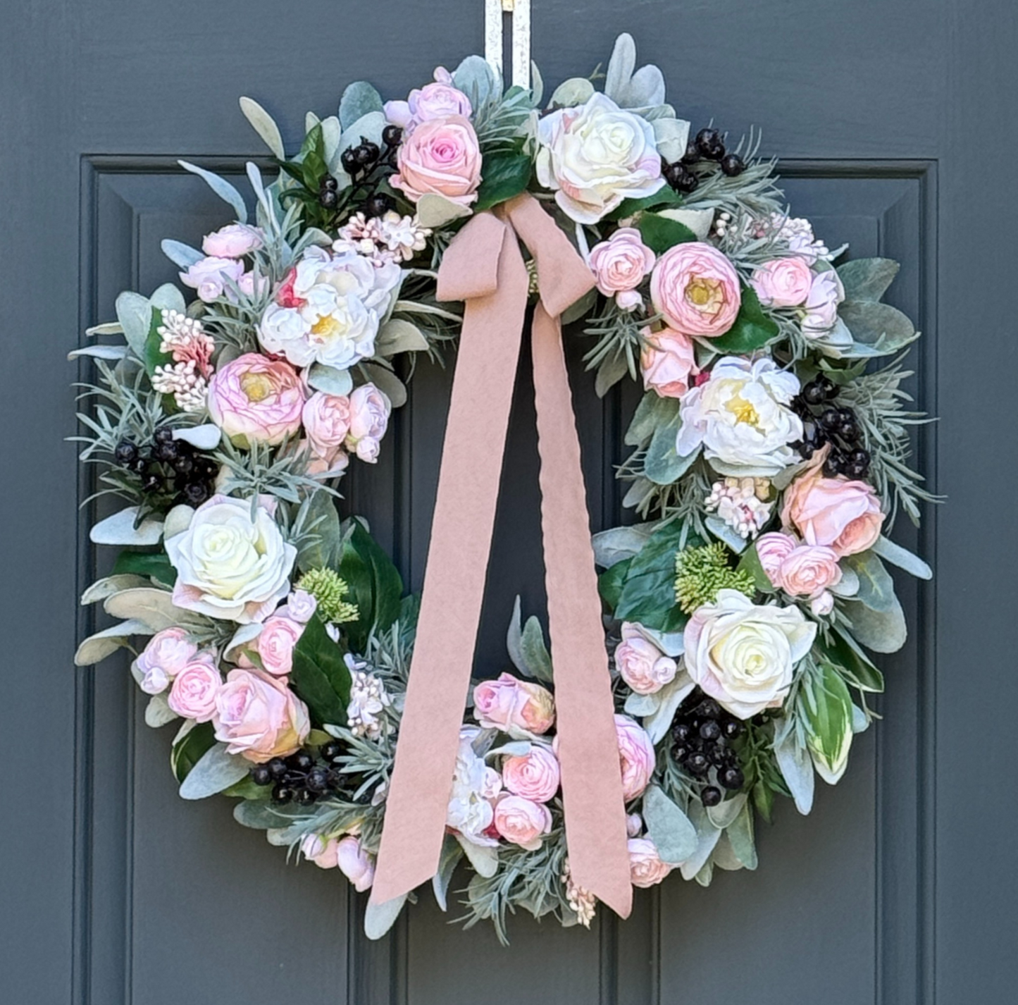 Peony, rose, and ranunculus wreath with pink and cream flowers, greenery, navy berries, and ribbon on an 18-inch grapevine base.