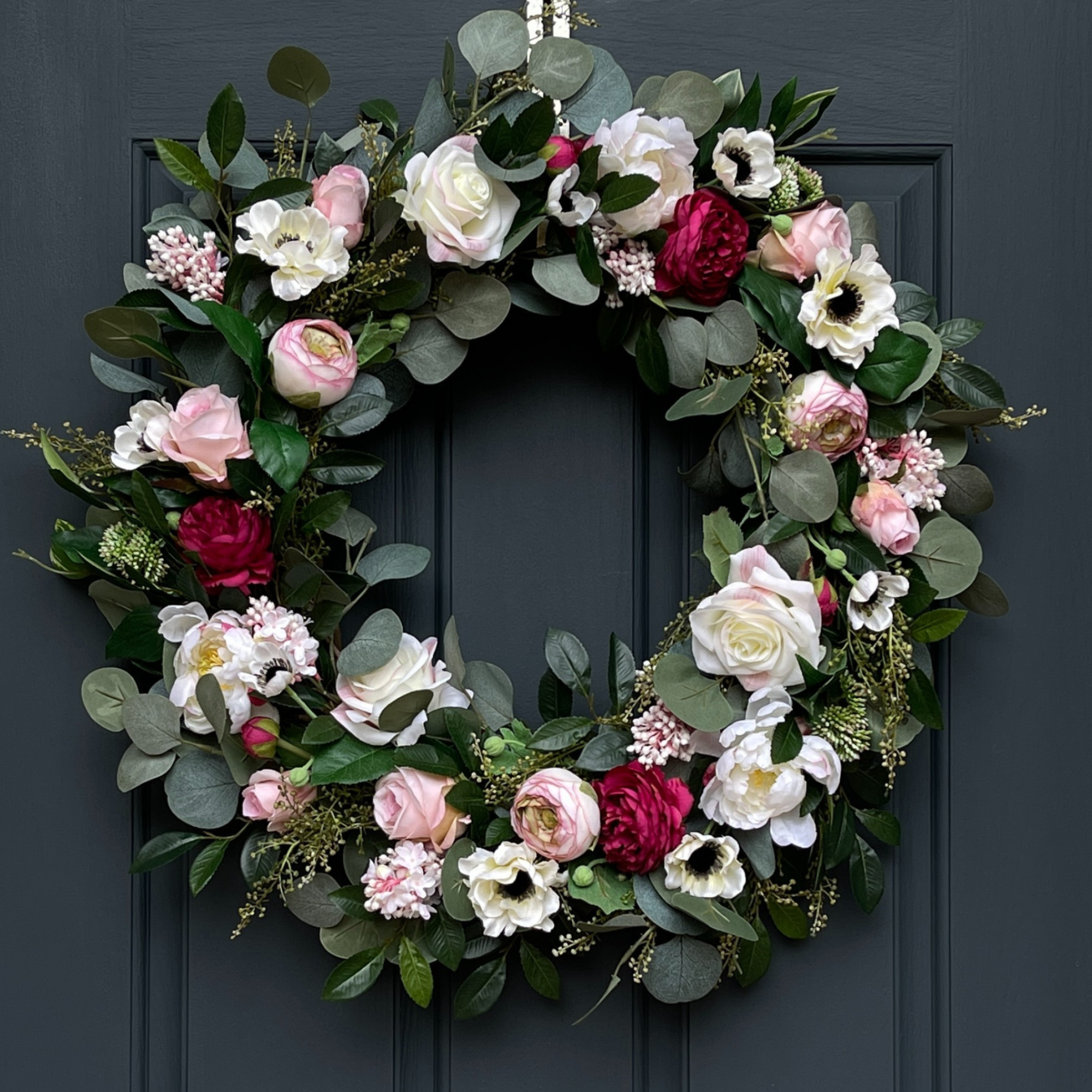 Pink and cream floral wreath with peonies, roses, ranunculus, anemones, and eucalyptus on a grapevine base for summer front door décor.