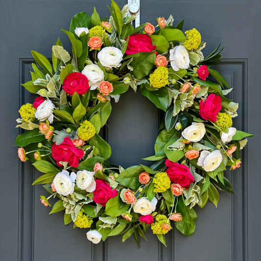 Floral wreath with bright pink, white, and peach flowers, with lime green snowball accents on a dark blue door.