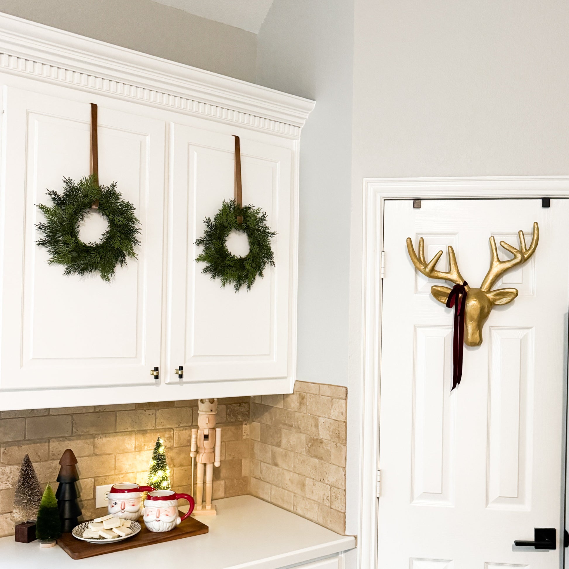 Kitchen with white cabinets, mini cedar Christmas wreaths on the cabinets, and a reindeer head mount.