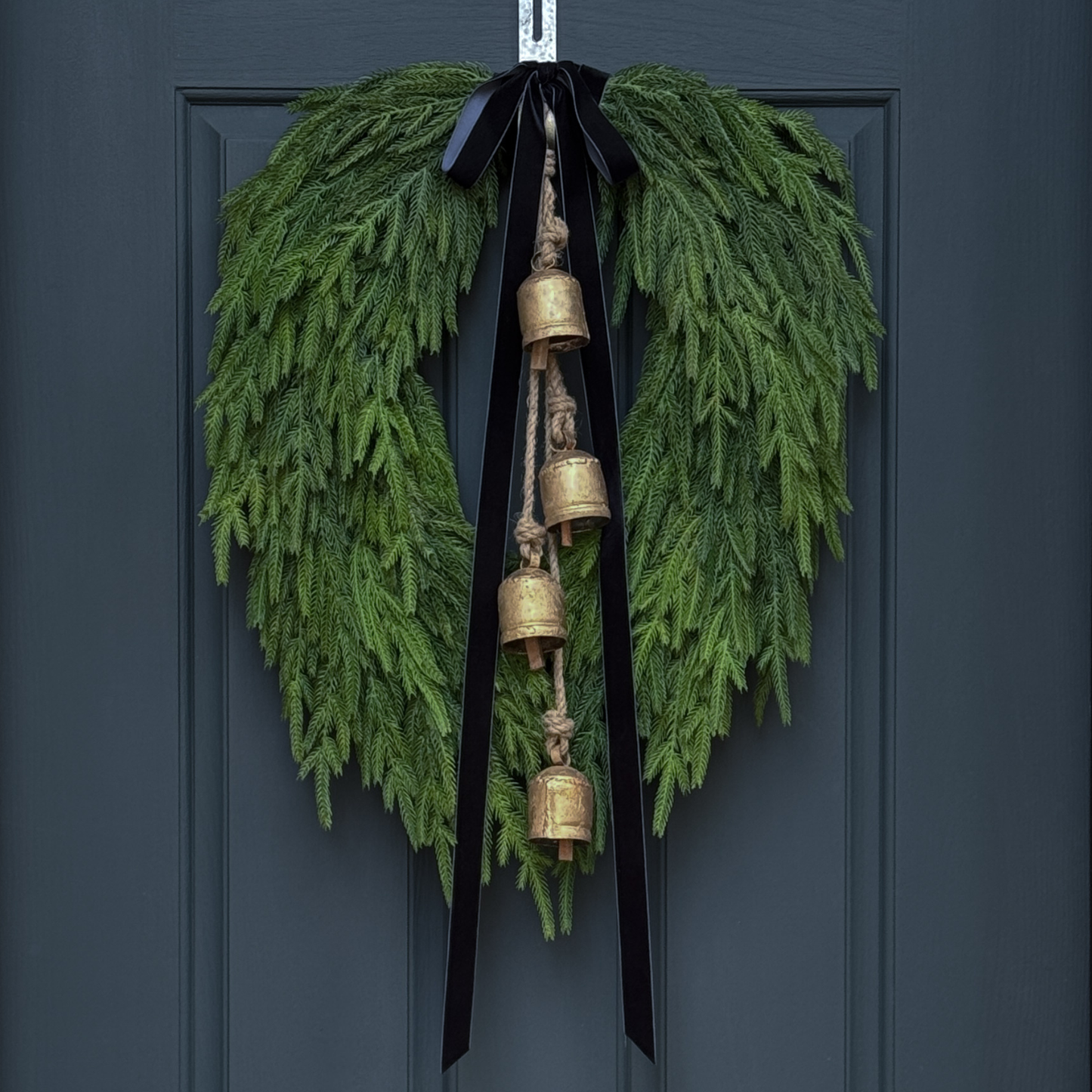 Green wreath with gold bells and black ribbon on a dark blue door