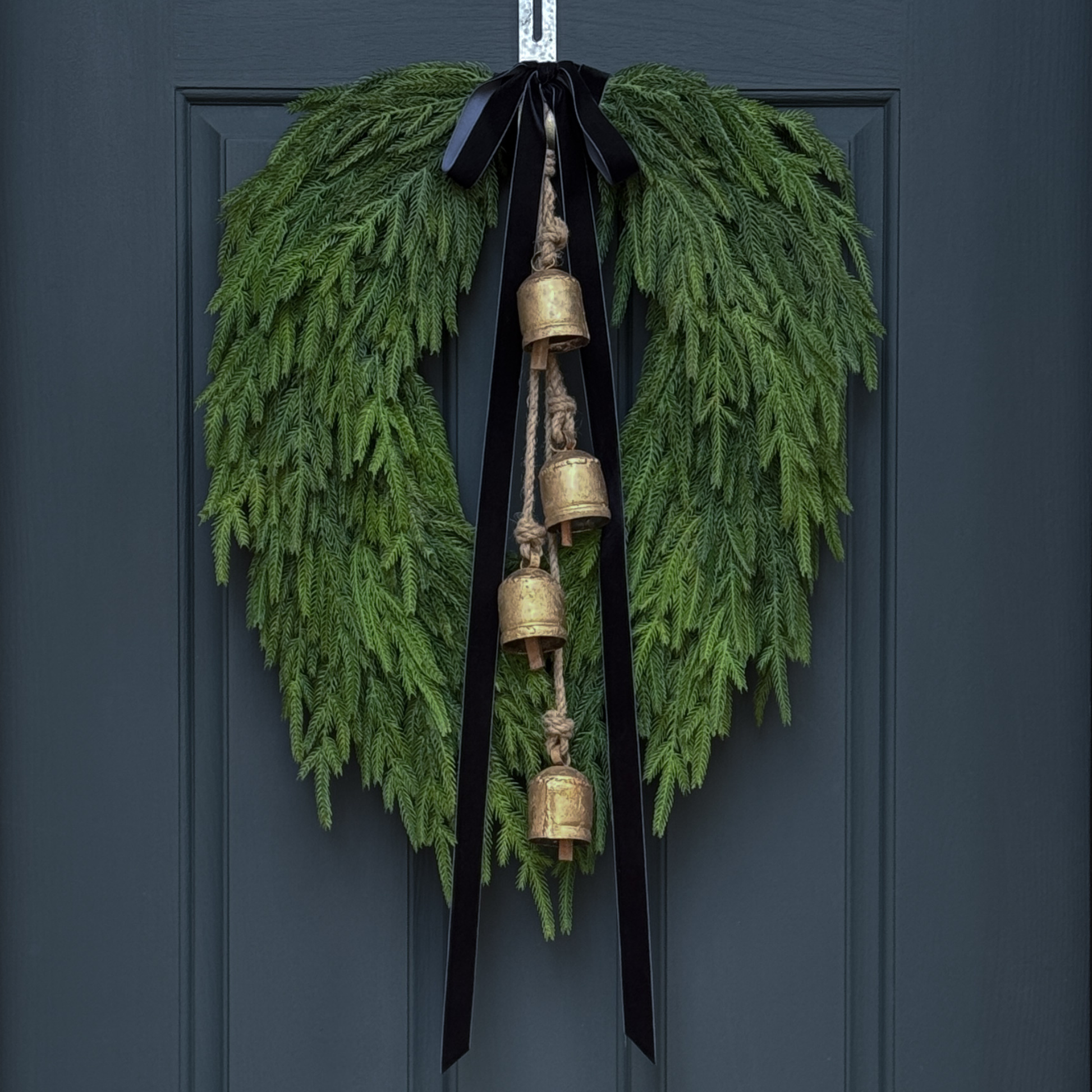 Green wreath with gold bells and black ribbon on a dark blue door