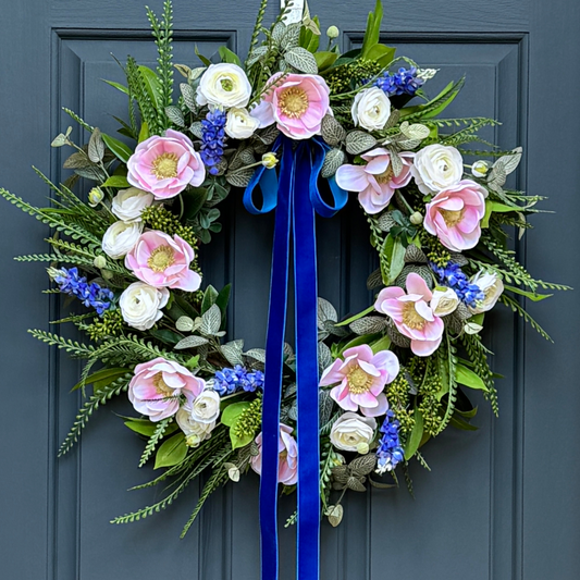 Floral wreath with pink, blue, and white flowers and a blue ribbon on a blue door.