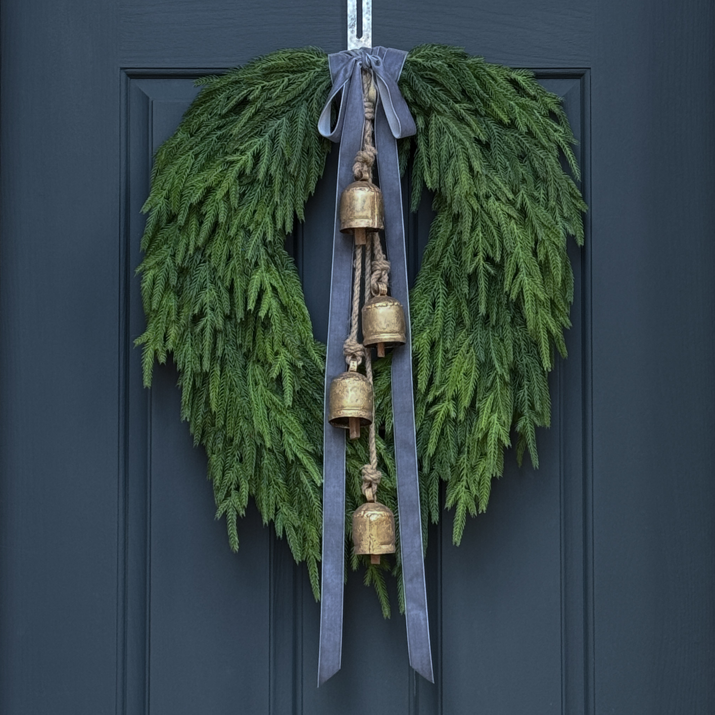Green wreath with gold bells and gray ribbons on a dark blue door