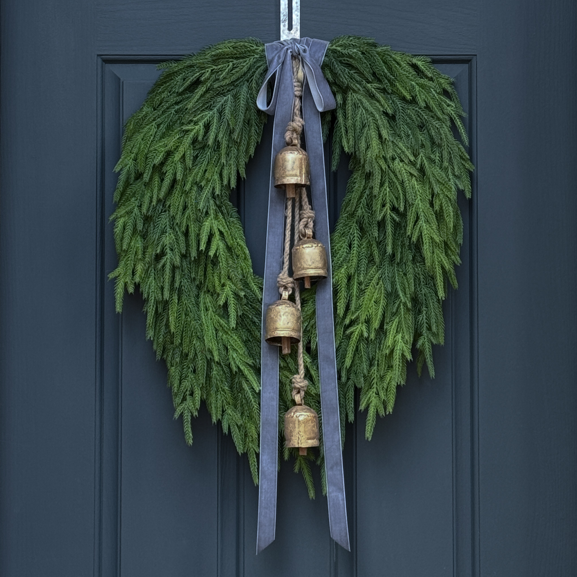 Green wreath with gold bells and gray ribbons on a dark blue door