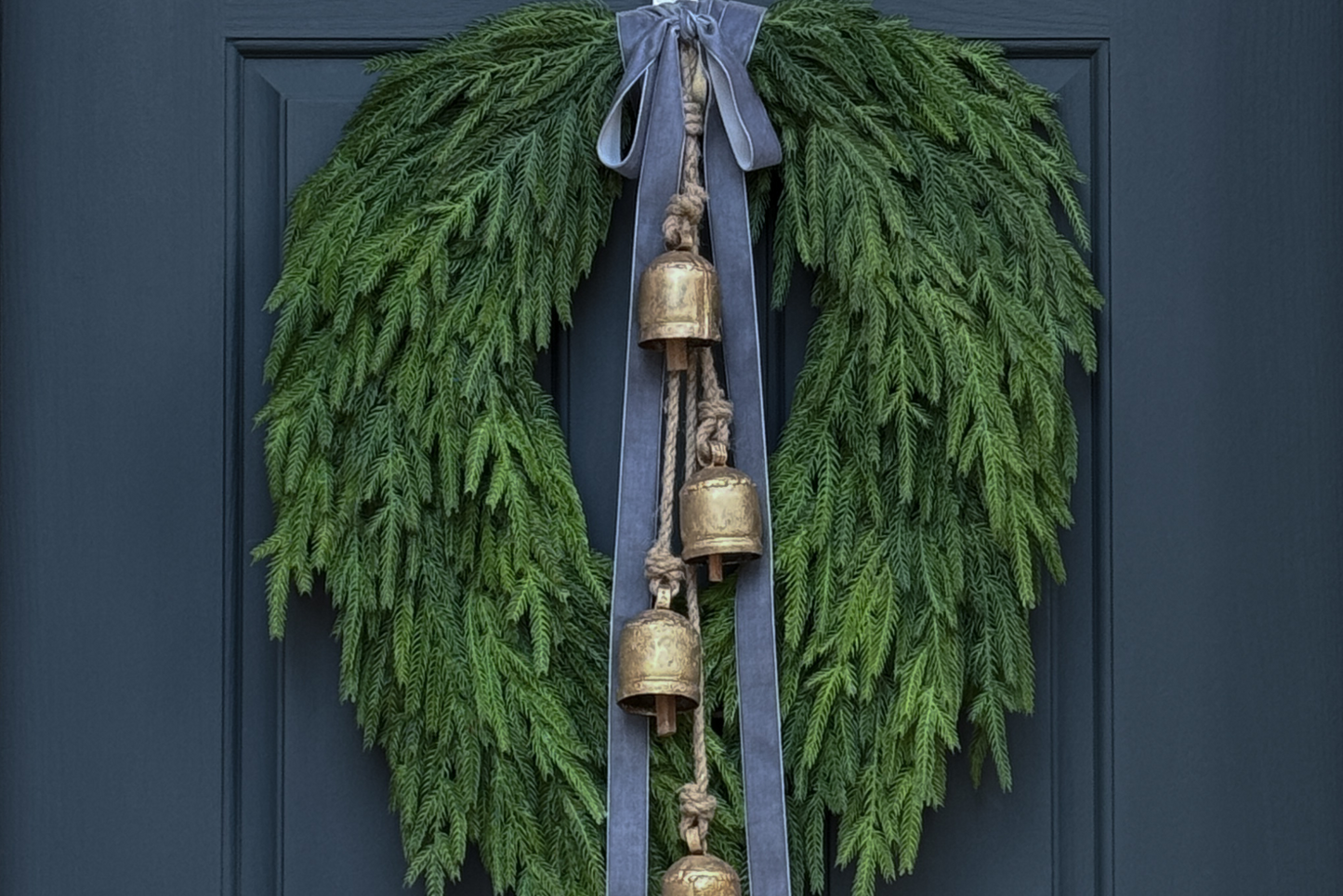 Green wreath with gold bells and gray ribbons on a dark blue door