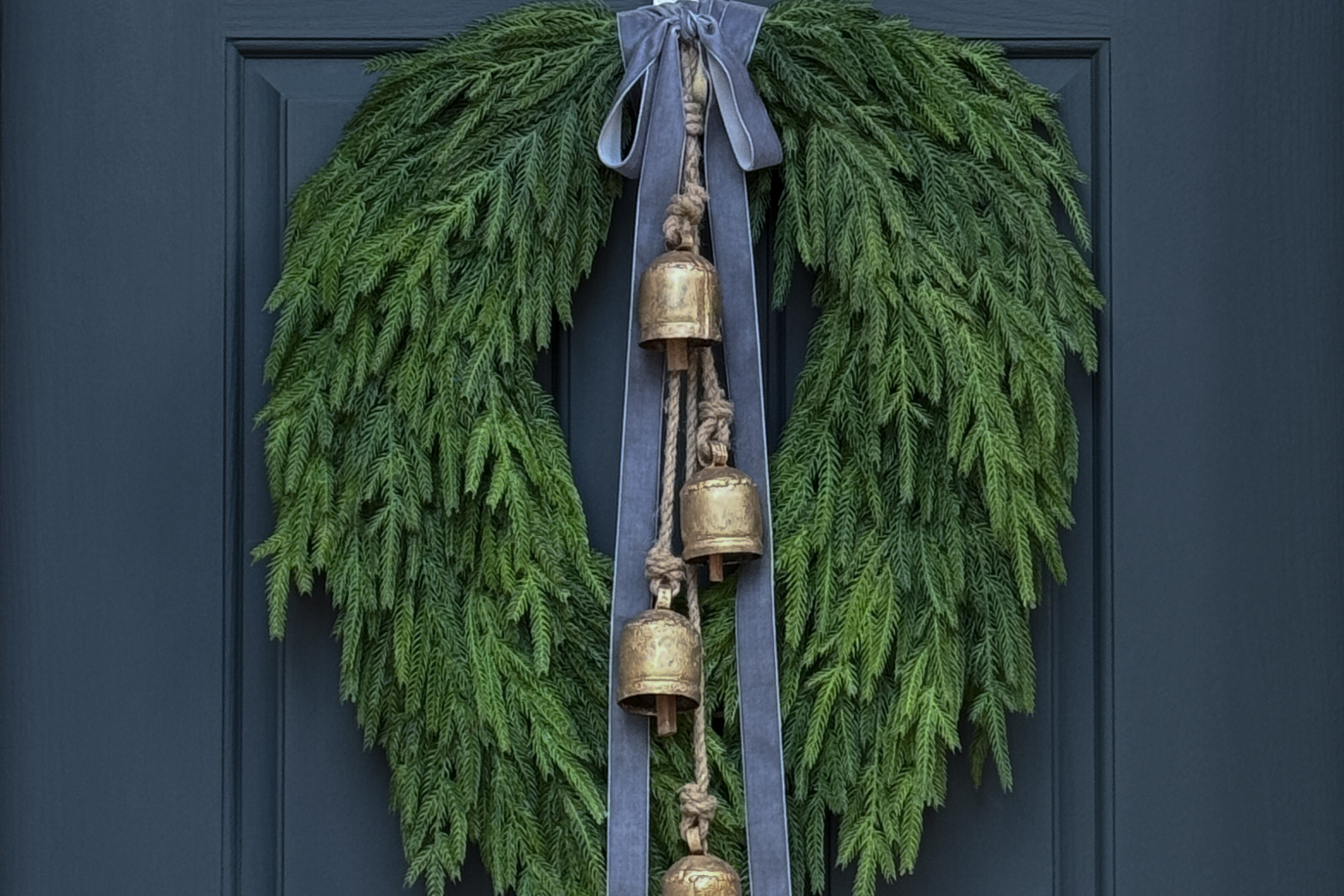Green wreath with gold bells and gray ribbons on a dark blue door