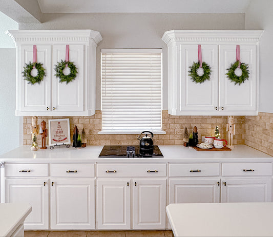 Kitchen with white cabinets, mini cedar Christmas wreaths, and a kettle on the stove.