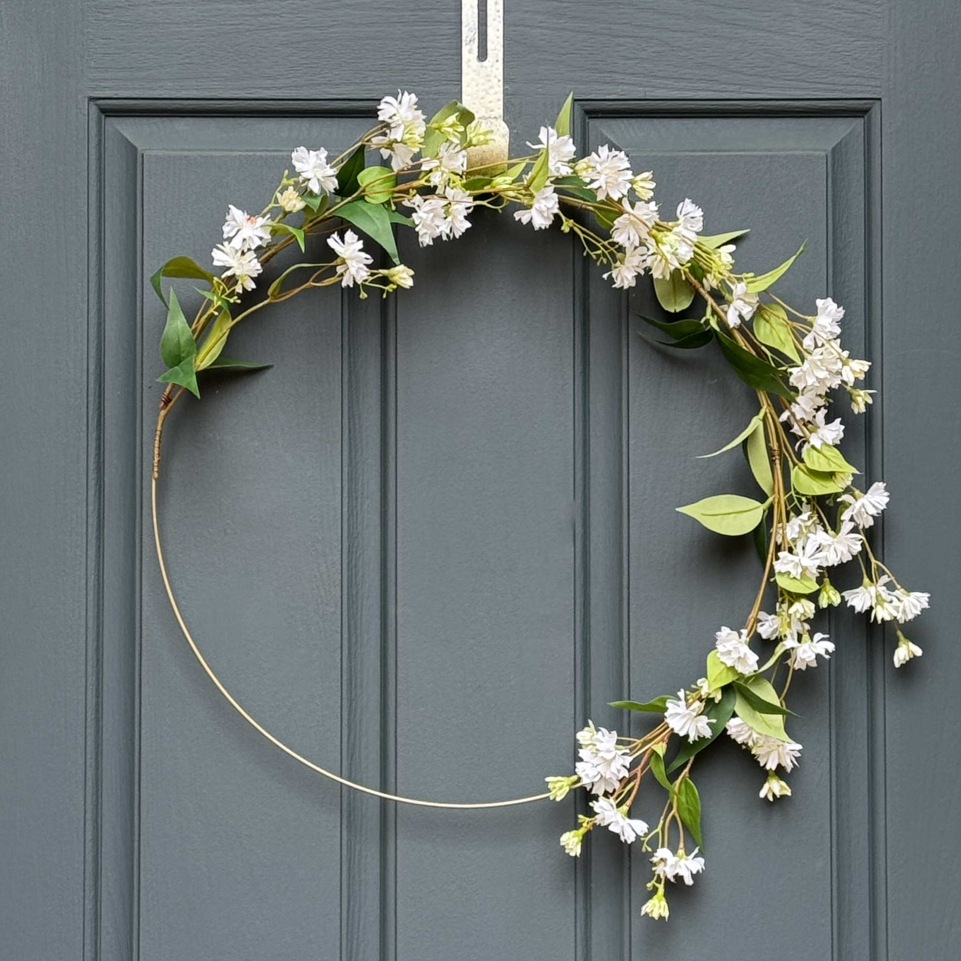 Floral wreath with white flowers and green leaves on a gray door