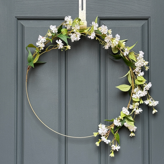 Floral wreath with white flowers and green leaves on a gray door