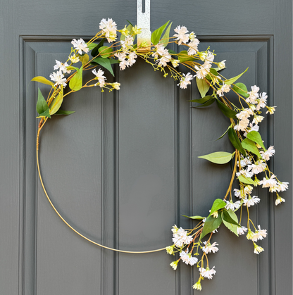 Floral hoop wreath with white flowers and green leaves hanging on a gray door.