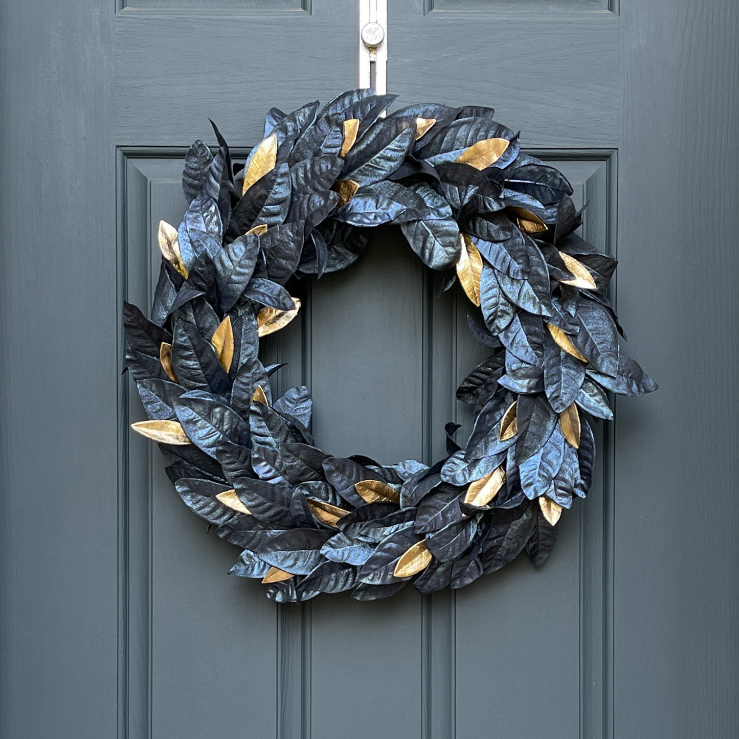 24" Halloween wreath featuring metallic black and gold leaves hanging on a dark blue door from a gold wreath hanger