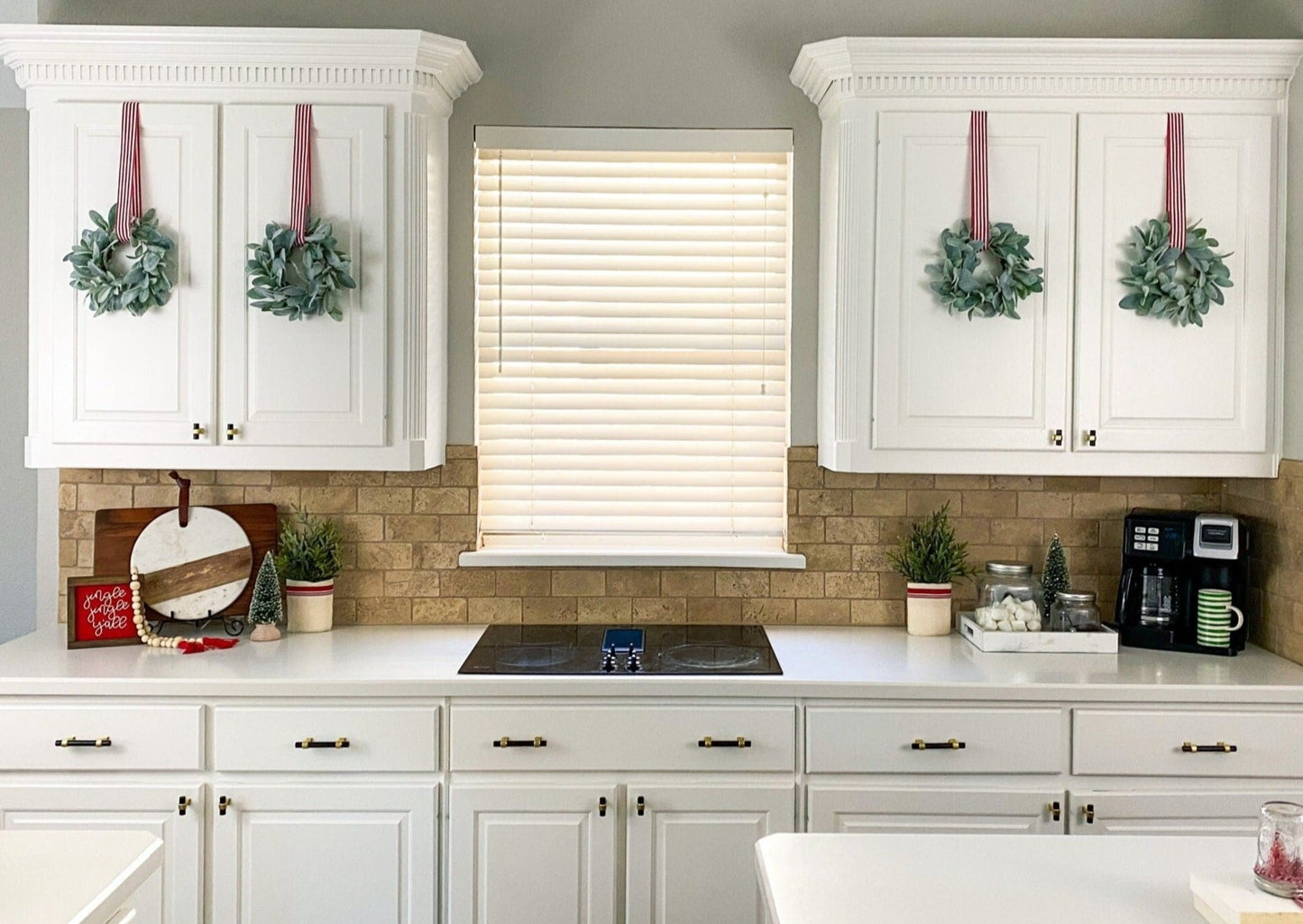 Four 11" grapevine wreaths with flocked lambs ear greenery on white kitchen cabinets, hung using 1.5 inch red and white stripped ribbon.