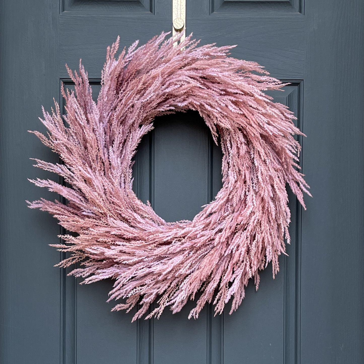 27" modern fall boho wreath, featuring artificial pink flocked pampas grass hanging from a gold wreath hanger on a dark blue door