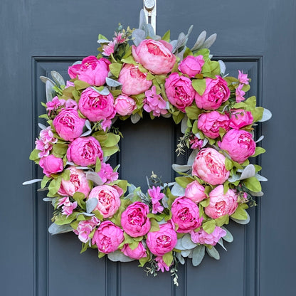 24" wreath has been handcrafted on a grapevine base and is trimmed with peonies in two shades of pink peonies (pale pink & bright pink), hydrangeas, and other floral accents on a bed of flocked lambs ear.